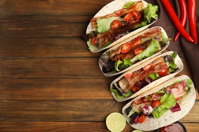 Photo of Delicious tacos with fried bacon, lime and chili pepper on wooden table, flat lay. Space for text