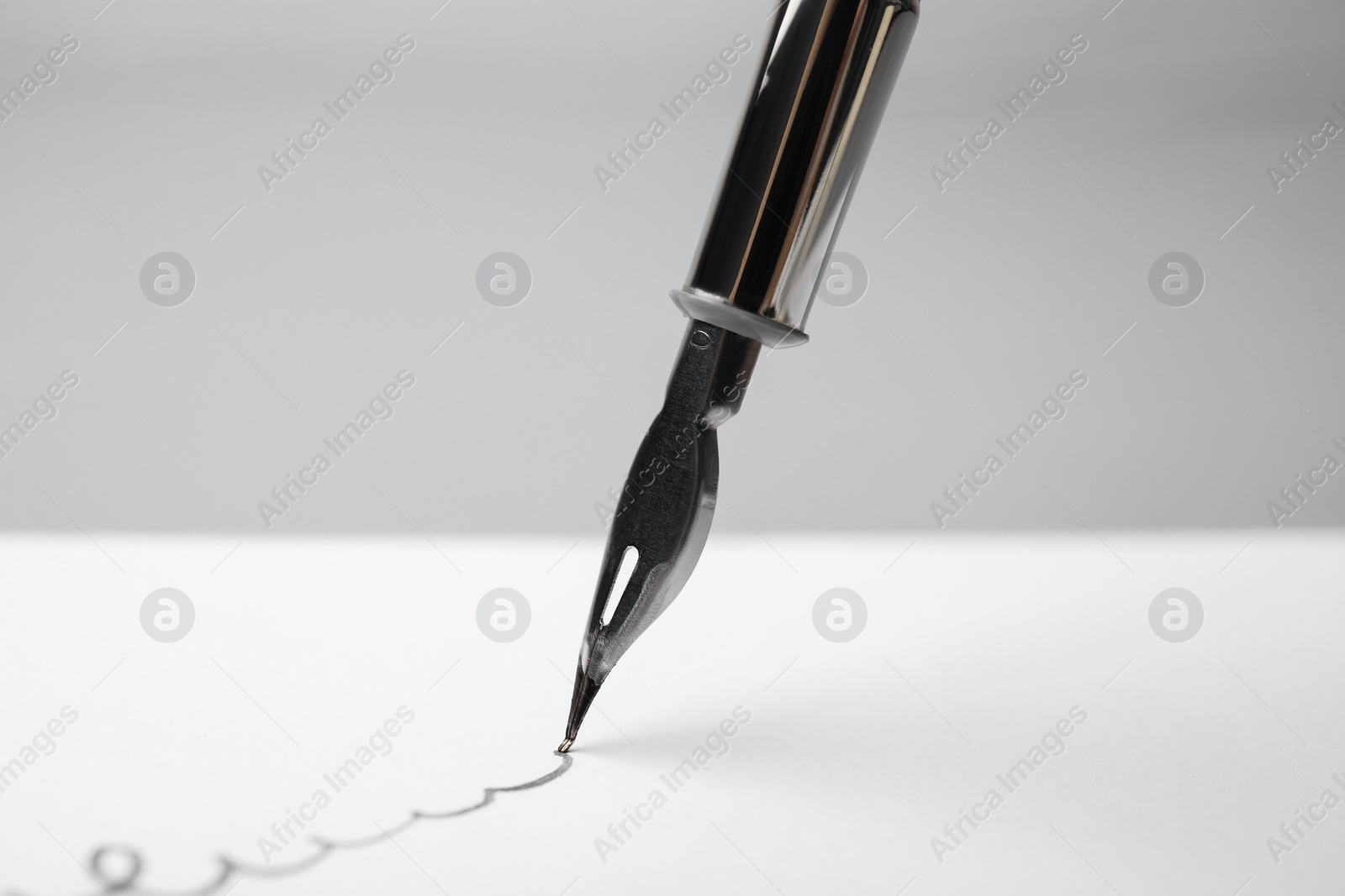 Photo of Signing on sheet of paper with fountain pen against light grey background, closeup