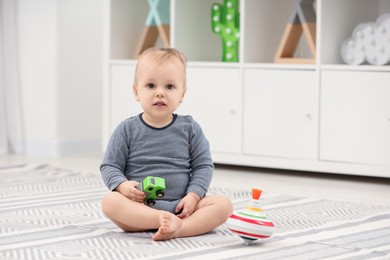 Photo of Children toys. Cute little boy with toy car and spinning top on rug at home