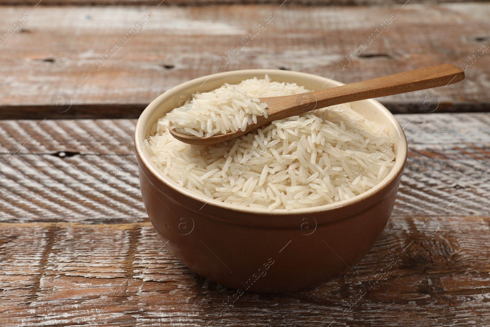 Photo of Raw basmati rice and spoon in bowl on wooden table