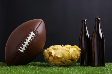 Photo of American football ball with potato chips and beer on green grass