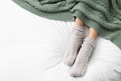 Photo of Woman wearing warm socks in comfortable bed, above view. Space for text