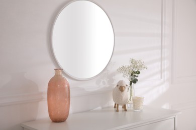 Photo of Trendy round mirror and chest of drawers with accessories near white wall. Interior element