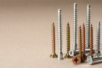 Many metal screws on beige background, space for text