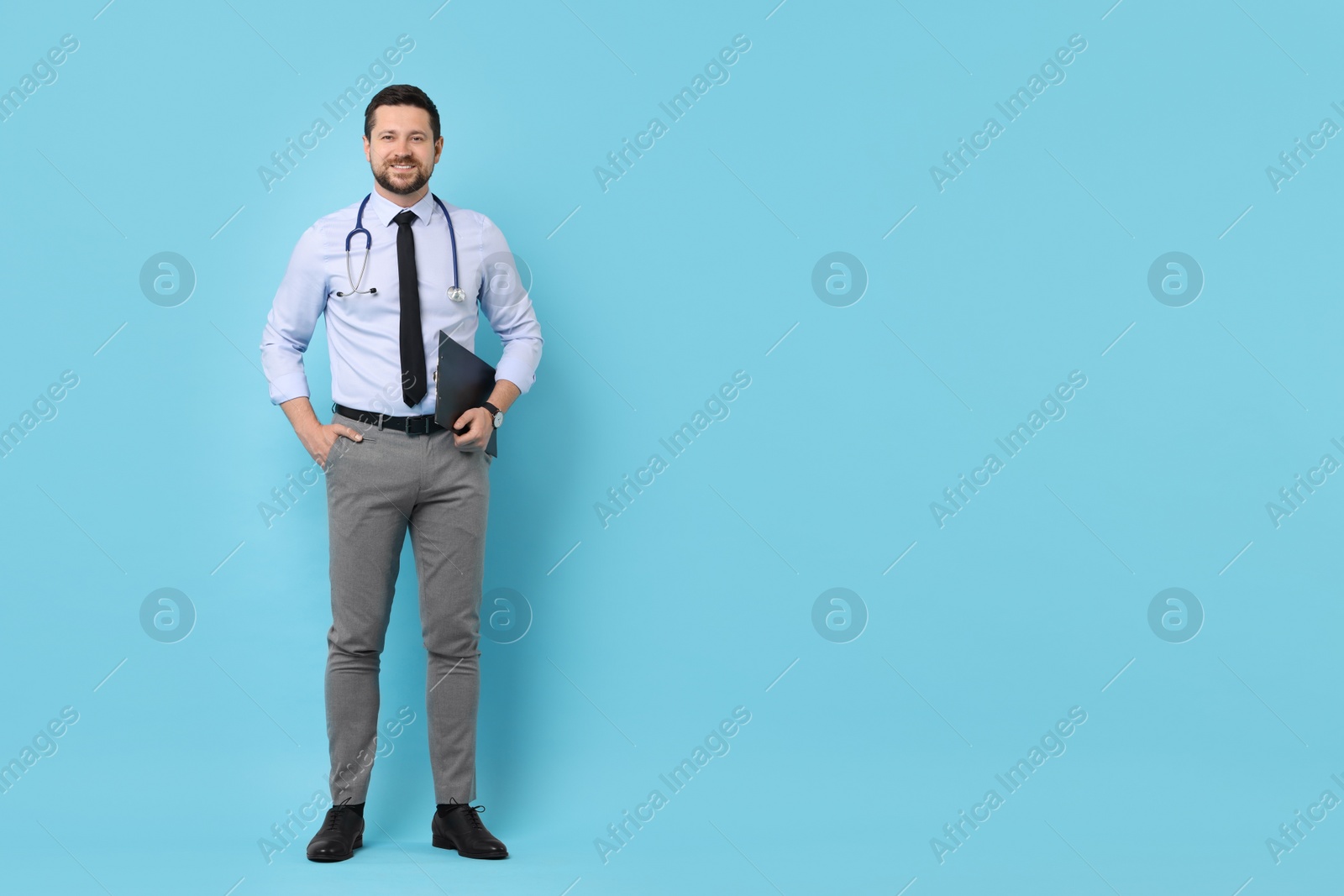 Photo of Smiling doctor with clipboard on light blue background. Space for text