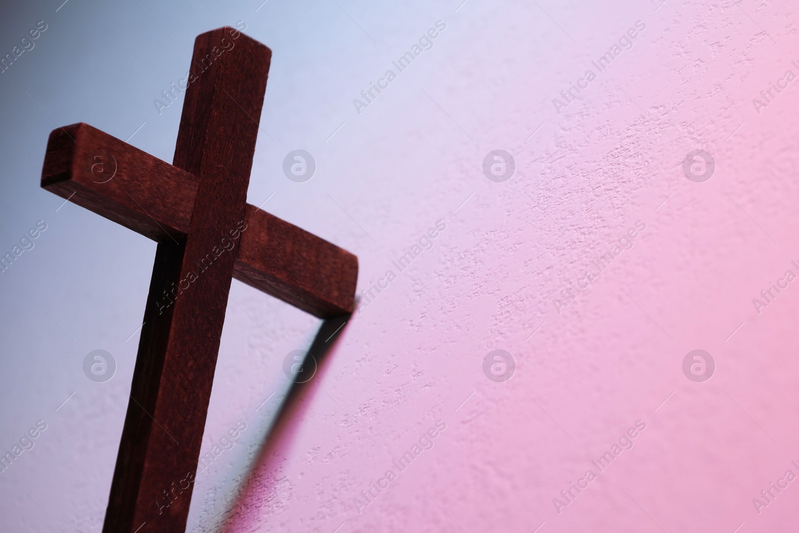 Photo of Wooden cross on textured table in color lights, closeup with space for text. Religion of Christianity