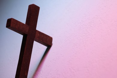 Wooden cross on textured table in color lights, closeup with space for text. Religion of Christianity