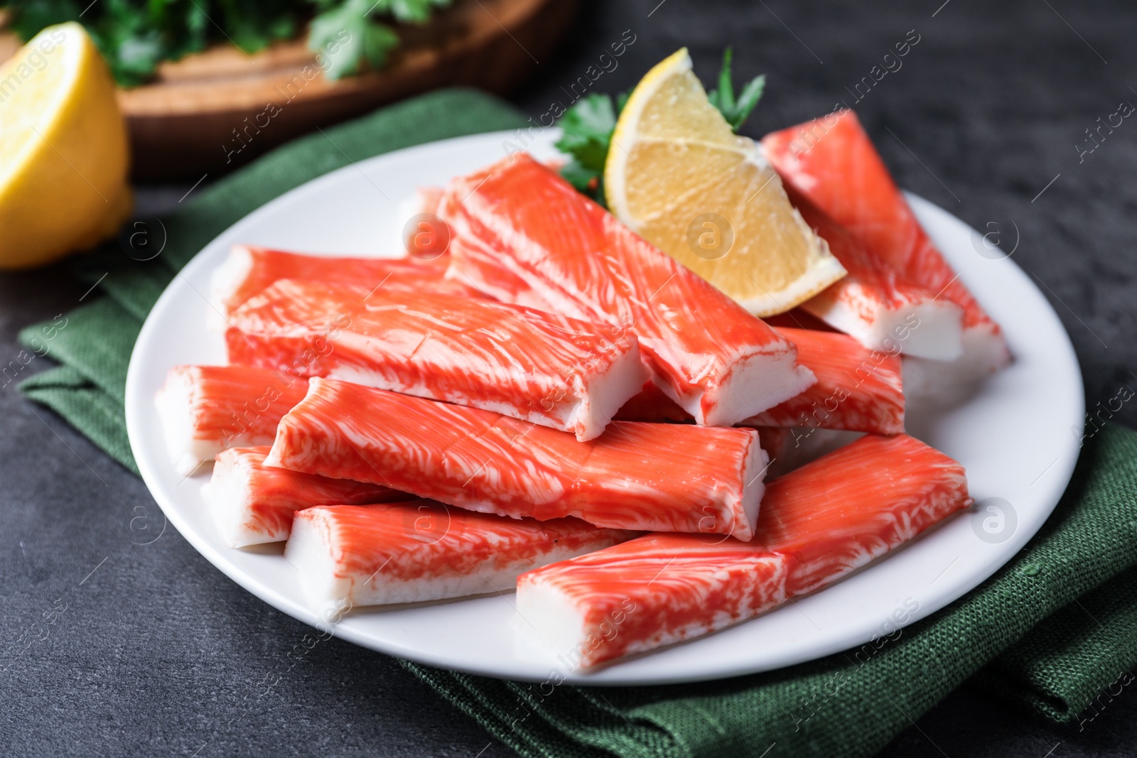 Photo of Plate of fresh crab sticks with lemon on grey table, closeup