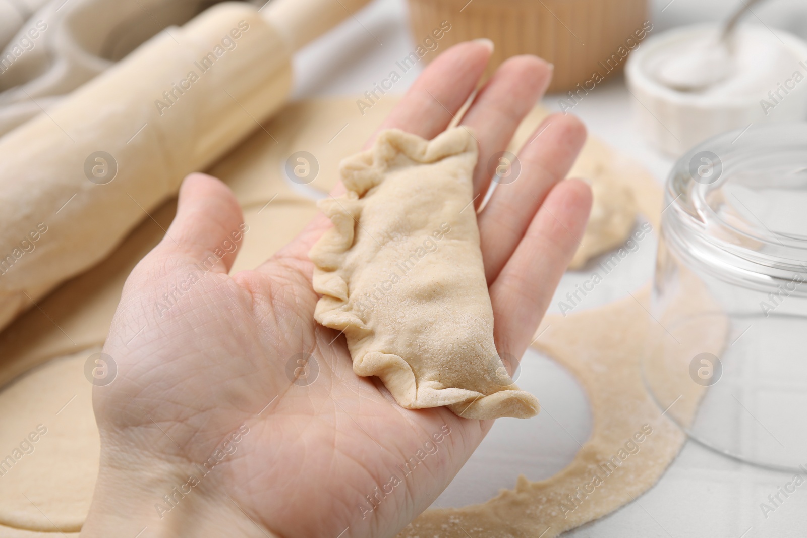 Photo of Woman holding dumplings (varenyky) with cottage cheese at white table, closeup