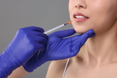 Woman getting lip injection on grey background, closeup