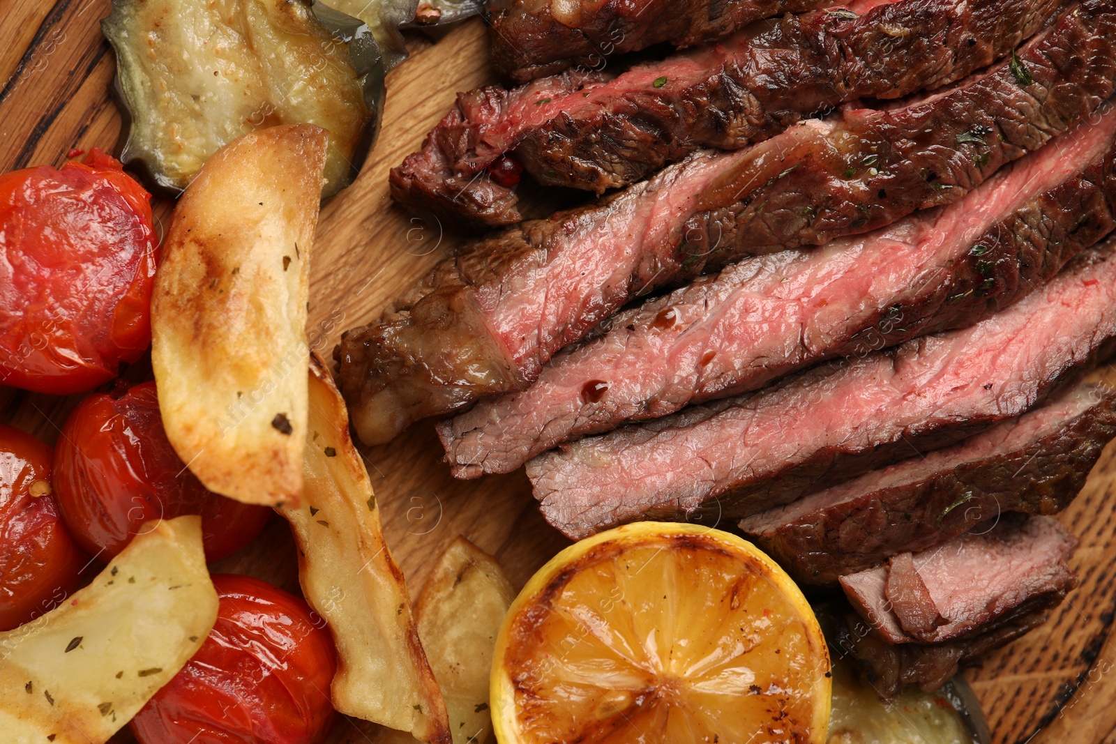 Photo of Delicious grilled beef with vegetables, lemon and spices on table, top view