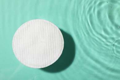 Photo of Cotton pad and micellar water on turquoise background, top view. Space for text