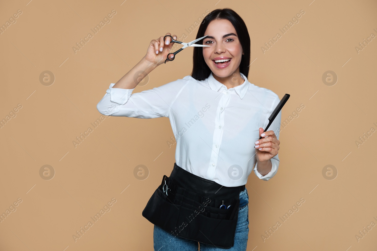 Photo of Portrait of happy hairdresser with professional scissors and comb on beige background