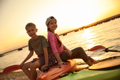 Photo of Happy children sitting on kayak near river at sunset. Summer camp