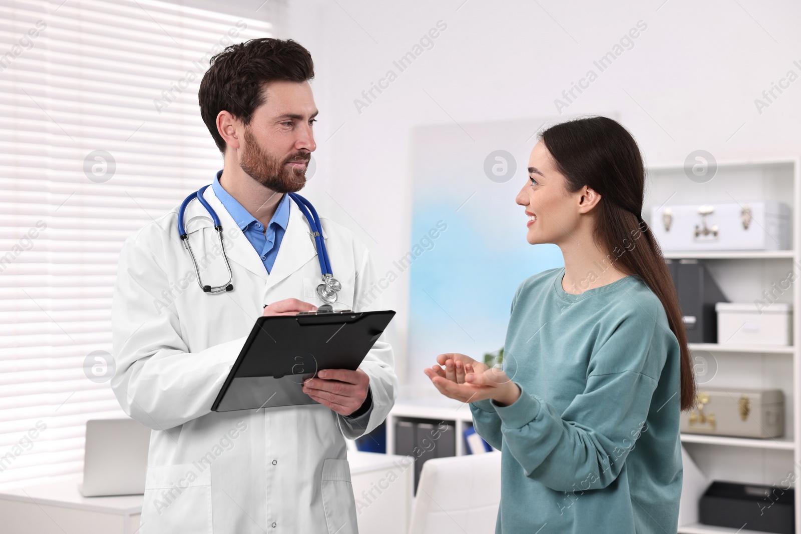 Photo of Doctor with clipboard consulting patient during appointment in clinic