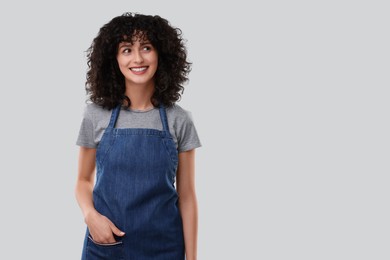 Happy woman wearing kitchen apron on light grey background, space for text. Mockup for design
