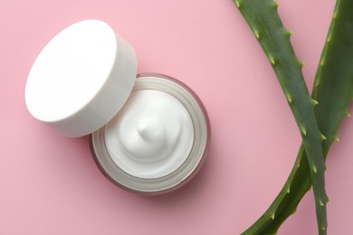 Jar with cream and aloe leaves on pink background, flat lay