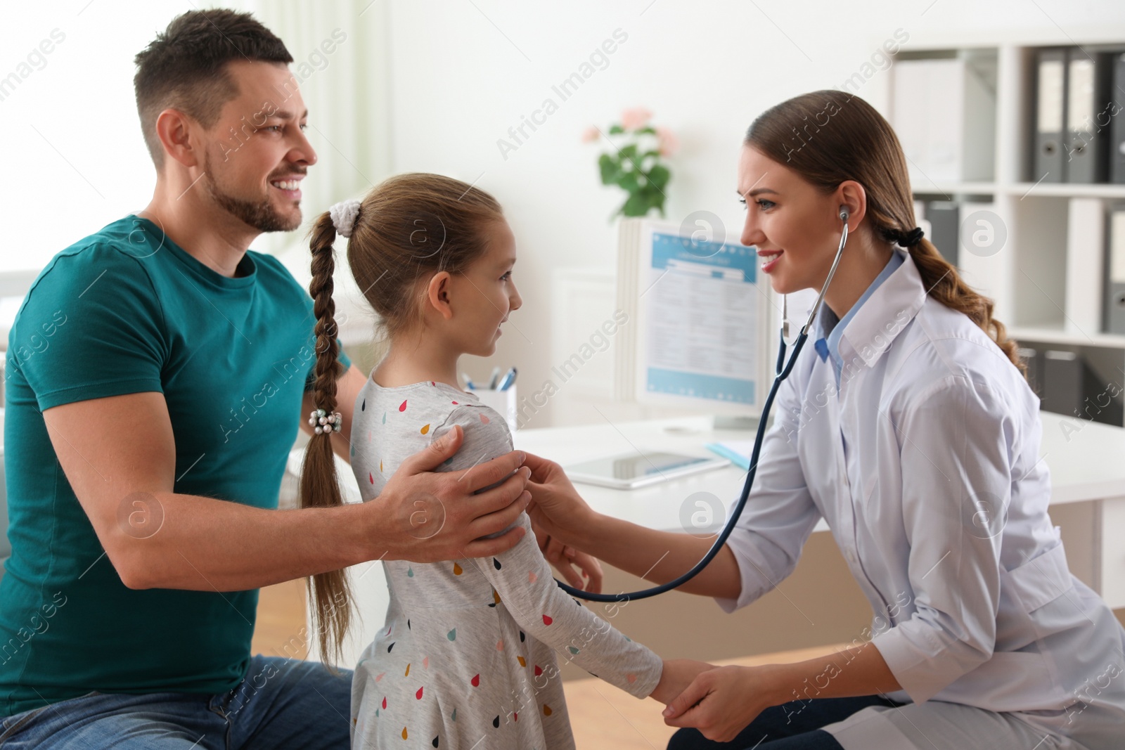 Photo of Father and daughter visiting pediatrician. Doctor examining little patient with stethoscope in hospital