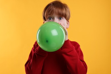 Photo of Boy inflating green balloon on orange background