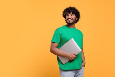 Smiling man with laptop on yellow background, space for text