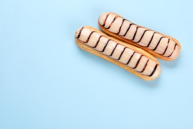 Delicious eclairs covered with glaze on light blue background, top view. Space for text