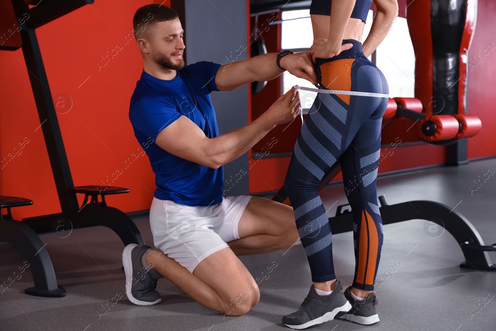 Photo of Trainer measuring woman`s hips with tape in gym