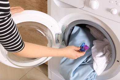 Woman putting laundry detergent capsule into washing machine indoors, closeup