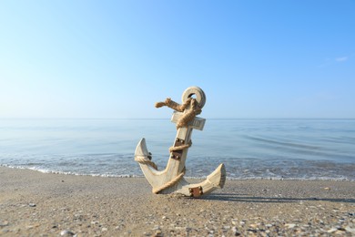 Photo of Wooden anchor with rope on sand near sea