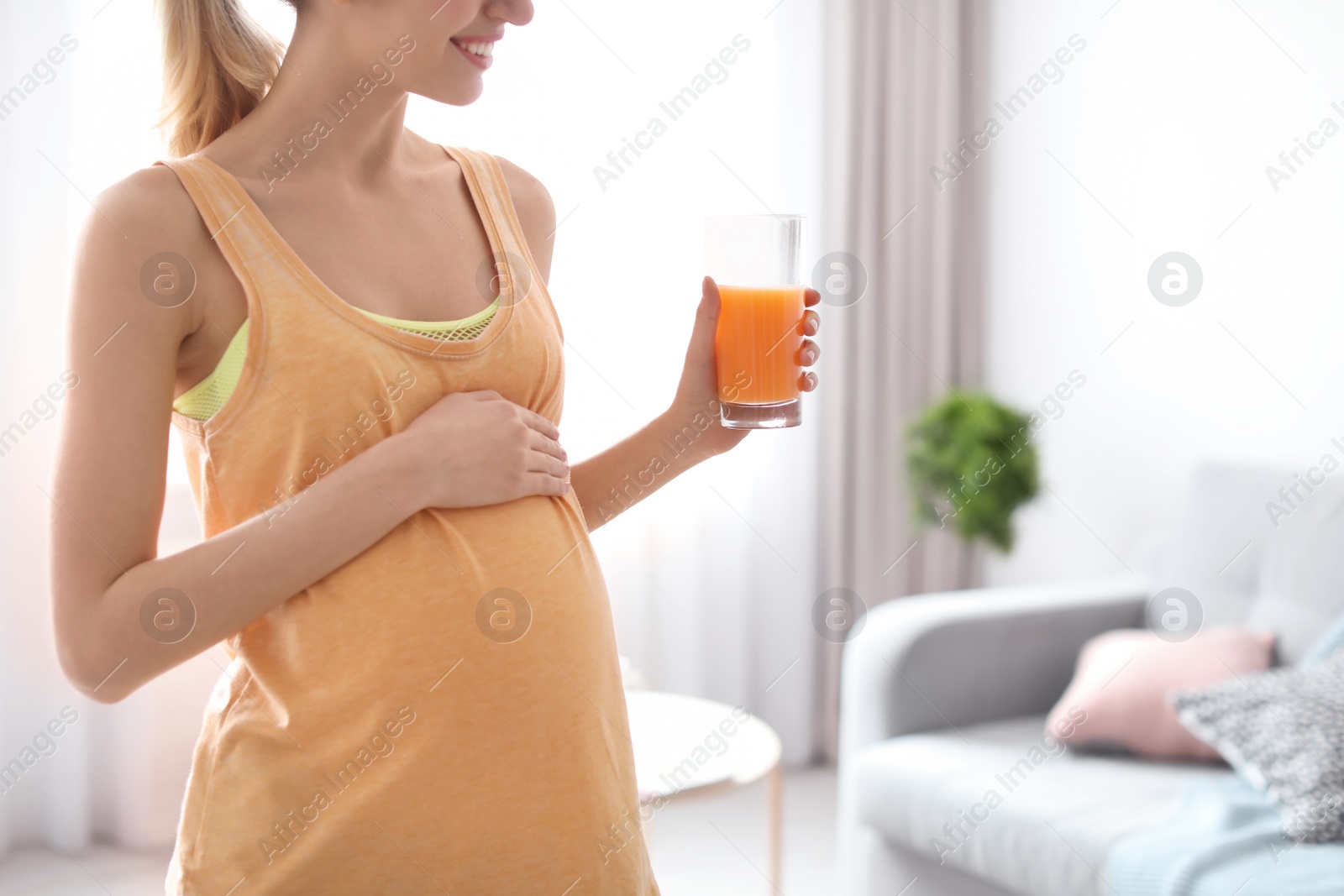 Photo of Young pregnant woman holding glass with juice at home