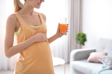 Young pregnant woman holding glass with juice at home