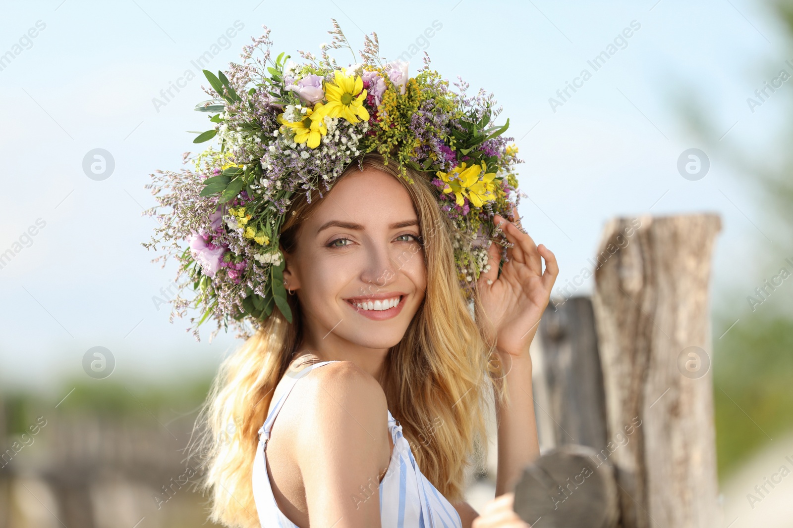 Photo of Young woman wearing wreath made of beautiful flowers outdoors on sunny day