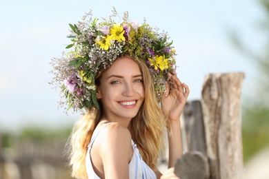 Young woman wearing wreath made of beautiful flowers outdoors on sunny day