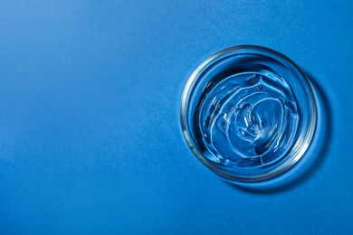 Photo of Petri dish with liquid on blue background, top view. Space for text