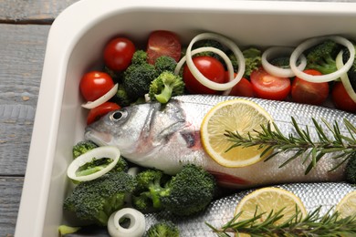 Photo of Raw fish with vegetables and lemon in baking dish on table