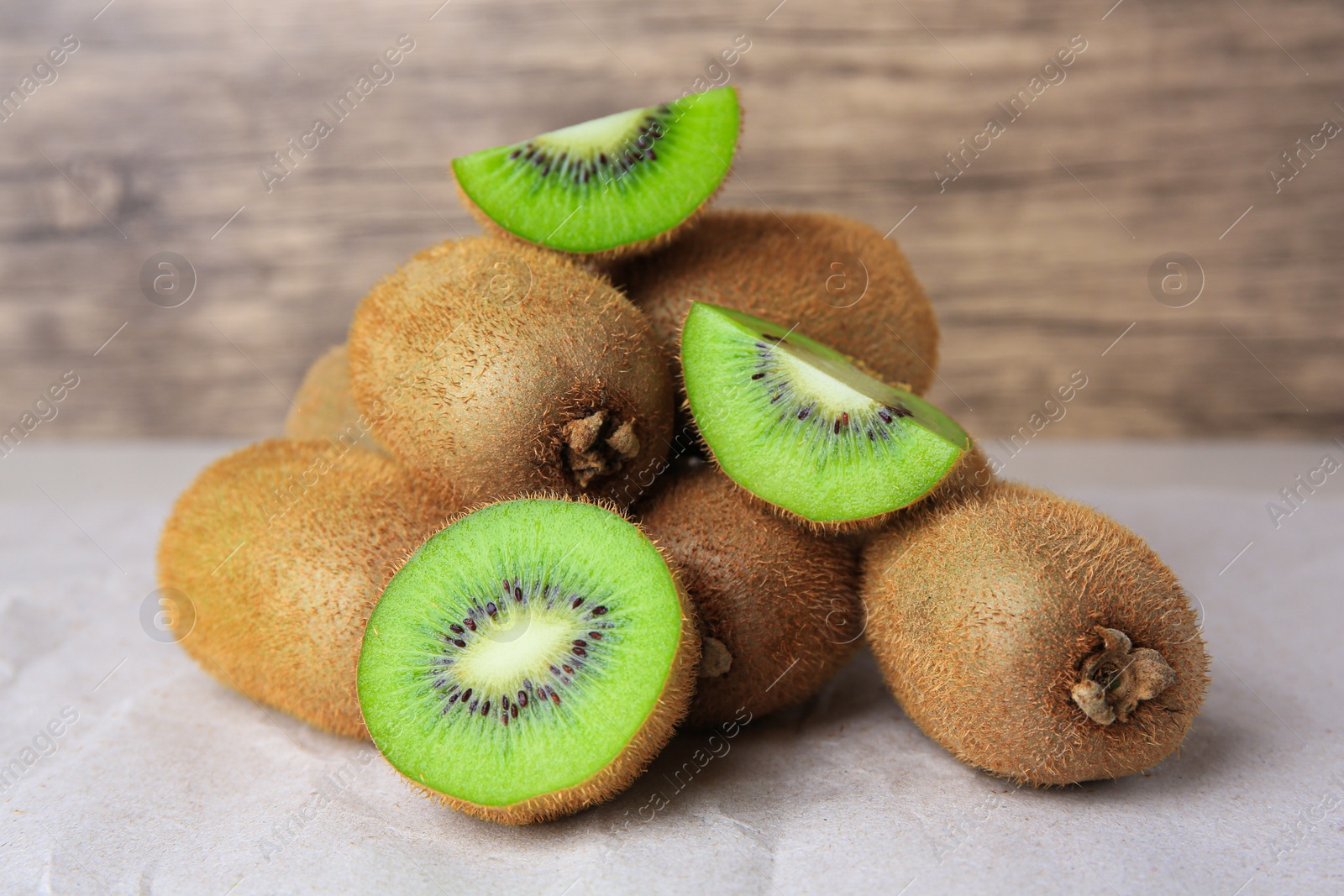 Photo of Heap of whole and cut fresh kiwis on parchment paper near wooden wall