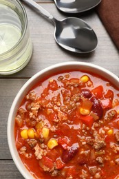 Photo of Bowl with tasty chili con carne served on wooden table, flat lay