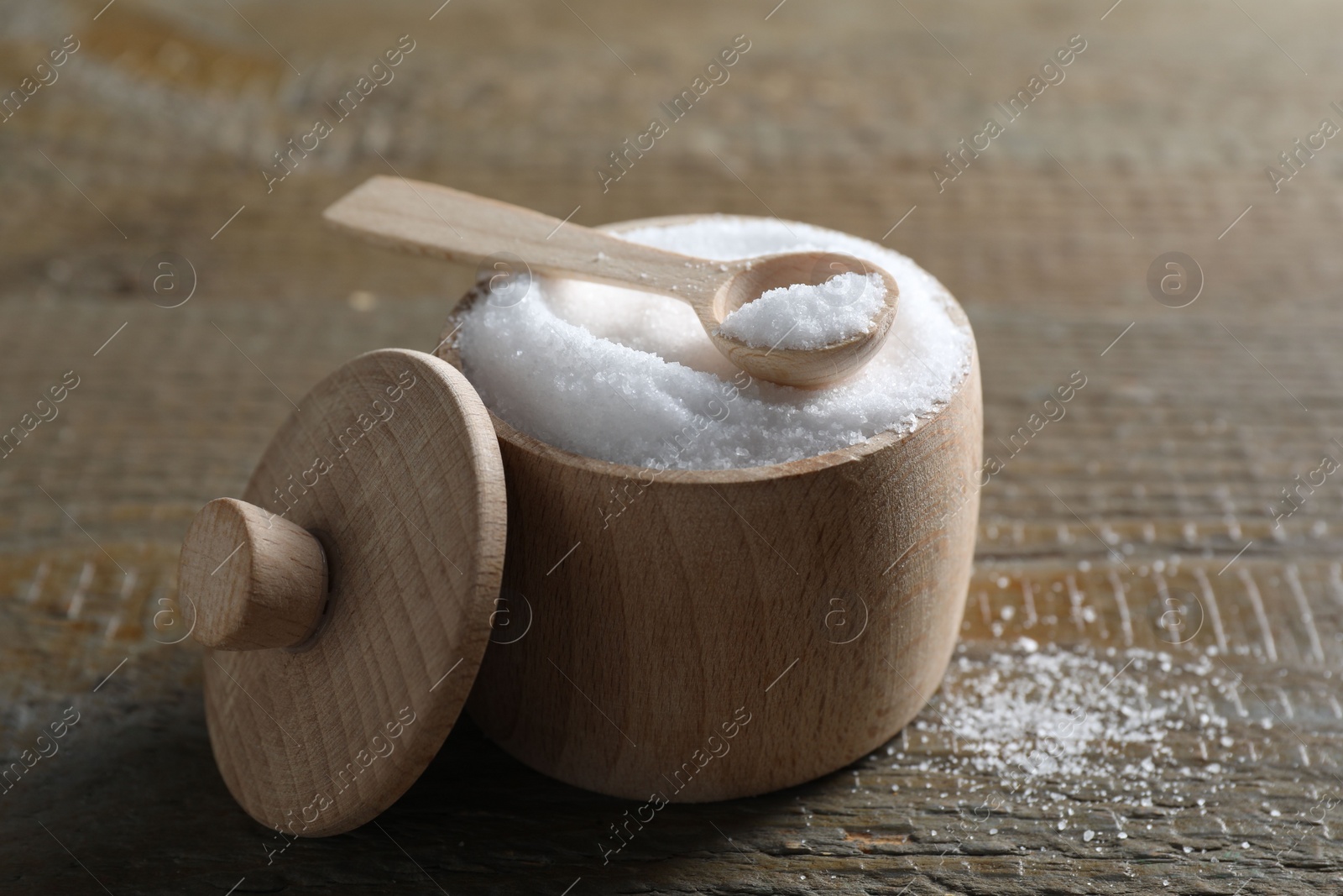 Photo of Organic salt in bowl and spoon on wooden table, closeup