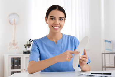 Photo of Young female orthopedist showing insole in clinic