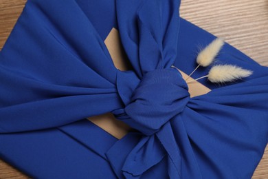 Furoshiki technique. Gift packed in blue fabric with dry flowers on wooden table, top view