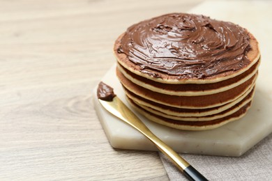 Photo of Delicious pancakes with chocolate paste and knife on wooden table, closeup. Space for text