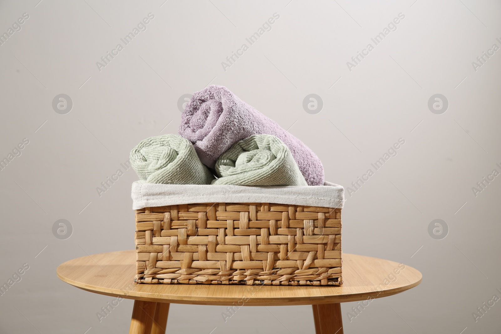 Photo of Clean towels in laundry basket on wooden table against gray background