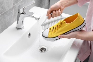 Photo of Woman washing stylish sneakers with brush in sink, closeup