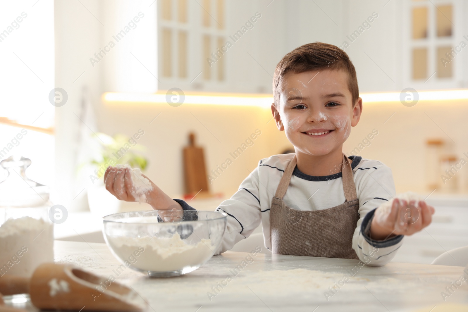 Photo of Cute little boy cooking dough at table in kitchen