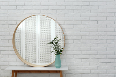 Photo of Round mirror and green plant near white brick wall