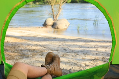 Photo of Young man resting in camping tent on riverbank, view from inside