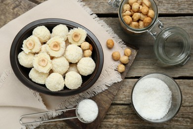 Delicious candies with coconut flakes, hazelnut and ingredients on wooden table, flat lay