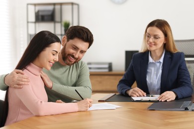 Photo of Happy couple signing document in lawyer's office, selective focus