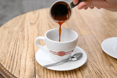 Photo of Woman pouring fresh coffee into cup at round wooden table, closeup