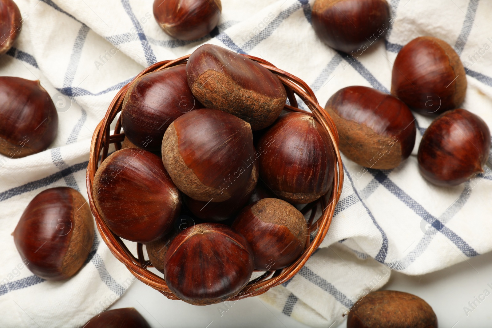 Photo of Sweet fresh edible chestnuts in wicker bowl on white table, top view