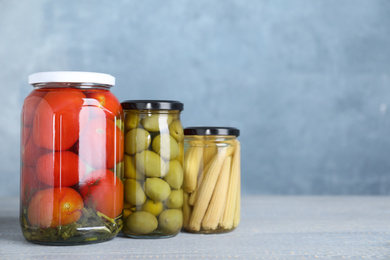 Photo of Glass jars with different pickled vegetables on table. Space for text